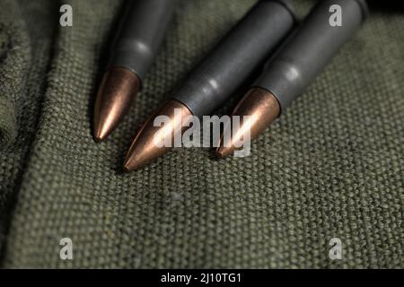 Three Ak-47 (7,62x39mm) cartridges lying on a piece of military canvas, close-up photography Stock Photo