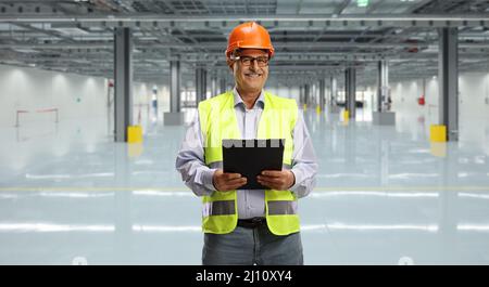 Male engineer with a reflective vest holding a clipboard inside a hall Stock Photo