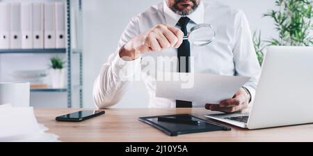 Tax inspector and financial auditor looking through magnifying glass, inspecting company financial papers, documents and reports, selective focus Stock Photo