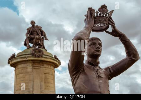 A statue of William Shakespeare's Prince Hal lifts a crown above his head watched over by a statue of the Bard himself. Stratford Upon Avon, England. Stock Photo