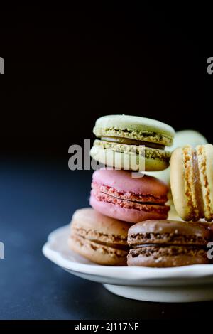 Pile of raspberry, pistachio, chocolate and lemon macaron cookies on a plate with a black background. Stock Photo