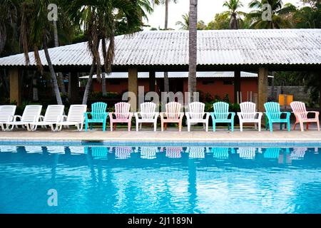 reflection of lined chairs in the swimming pool of a hotel. Empty seating outdoors in a exotic resort with palm trees Stock Photo