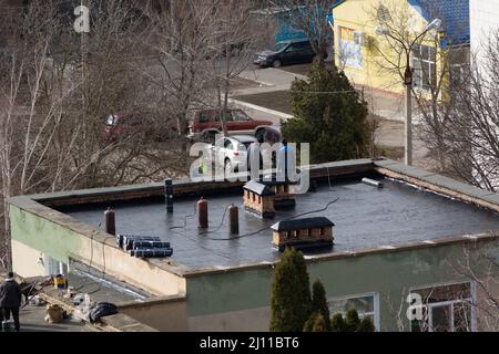 Tiraspol, Moldova - March 21, 2022: Cover the roof with bitumen. Workers cover the roof with bitumen of a kindergarten building. Stock Photo