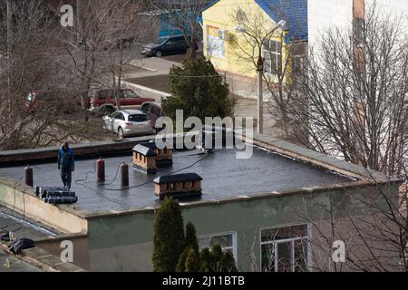 Tiraspol, Moldova - March 21, 2022: Cover the roof with bitumen. Workers cover the roof with bitumen of a kindergarten building. Stock Photo