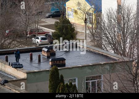 Tiraspol, Moldova - March 21, 2022: Cover the roof with bitumen. Workers cover the roof with bitumen of a kindergarten building. Stock Photo