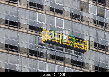Workers in a construction cradle at a height are engaged in glazing the facade of a skyscraper in winter. Side vie Stock Photo