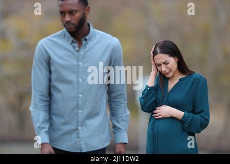 Front view portrait of a breakup with a husband leaving his sad pregnant wife in a park Stock Photo