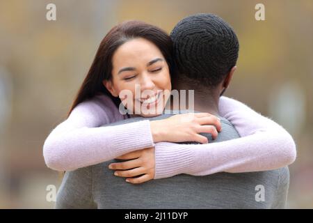 Front view portrait of a happy caucasian woman hugging a man with black skin in a park Stock Photo