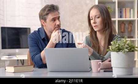 Business people working in office with laptop computer. Happy couple working from home at desk. Talking, meeting, cooperation, entrepreneurs, advisor. Stock Photo