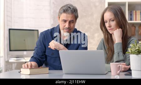 Business people working in office with laptop computer. Happy couple working from home at desk. Talking, meeting, cooperation, entrepreneurs, advisor. Stock Photo