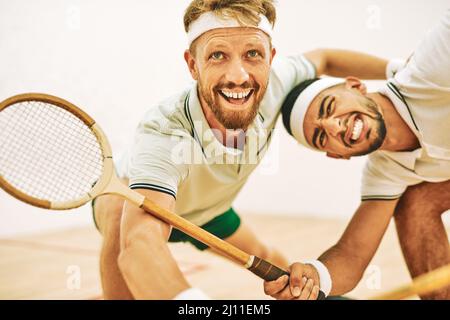 Hit the ball off the wall. Shot of two young men playing a game of squash. Stock Photo
