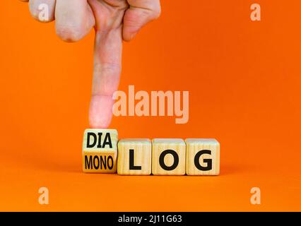 Businessman turns wooden cubes and changes the German word monolog - monologue in English to dialog - dialogue in English. Beautiful orange background Stock Photo