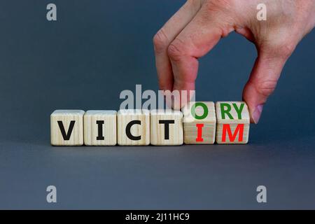 From victim to victory symbol. Businessman turns wooden cubes and changes concept words Victim to Victory. Beautiful grey background. Business support Stock Photo