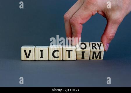 From victim to victory symbol. Businessman turns wooden cubes and changes concept words Victim to Victory. Beautiful grey background. Business support Stock Photo