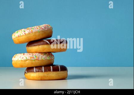 An uneven turret of four delicious fresh donuts sprinkled with different colors and with chocolate. Donuts only leash touch each other with one edge Stock Photo