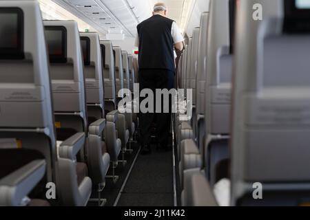 Male flight attendant serving meals to passengers on plane aisle. Anonymous man working on airplane Stock Photo