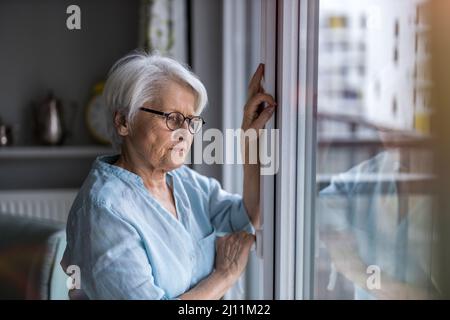 Senior woman looking out of window at home Stock Photo