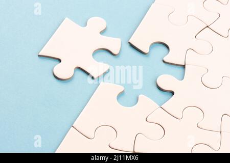 Puzzle edge piece on sky blue surface. White jigsaw game grid texture. Matching, inserting last missing part. Business and teamwork problem solving Stock Photo