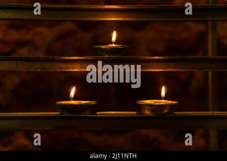 Three lit votive candles on a votive candle rack in a Catholic church. Stock Photo