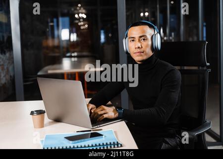 Handsome asian student with laptop and headphones is doing distance learning online. Remote work for programmers Stock Photo