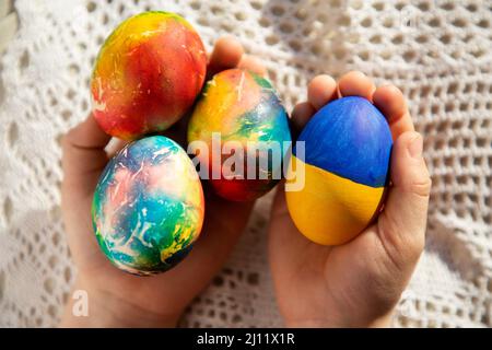 Easter festive composition - children's hands hold chicken eggs, one of which is painted in yellow-blue colors of the Ukrainian flag. Easter concept, Stock Photo