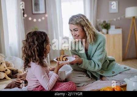Happy mother with her little daughter having breakfast together in bed at home. Stock Photo