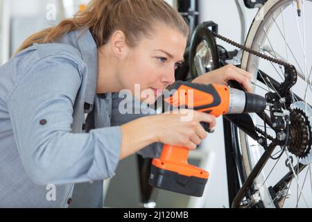 female mechanic working on bicycle chain using cordless screwdriver Stock Photo