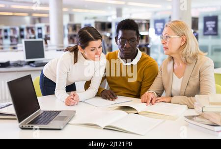 Students sitting in library, working with professor Stock Photo