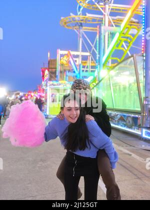 Two friends jumping on the back and joking while holding a cotton candy outdoors Stock Photo