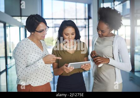 Putting their heads together. Cropped shot of three businesswomen looking at a tablet in the office. Stock Photo