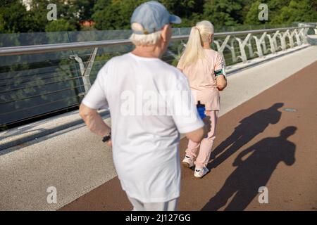 Pair of active pensioners runs together along footbridge on summer day backside view Stock Photo