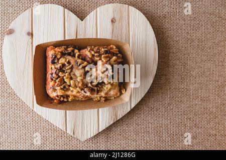 Walnut cinnamon roll close up on a wooden heart-shaped board, flat lay with copy space Stock Photo