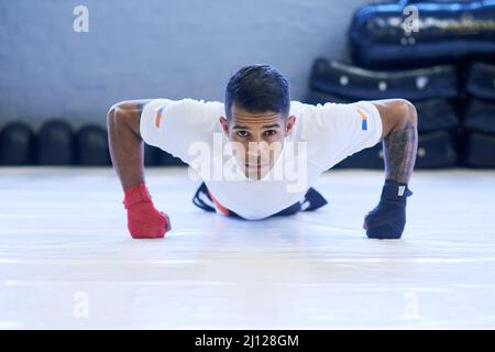 Building my strength for the next fight. Portrait of a young man doing pushups in the gym. Stock Photo
