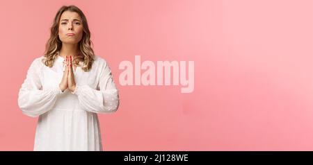 Portrait of hopeful clingy girlfriend, blond girl begging for favour in white dress over pink background, sobbing make cute eyes, pleading or praying Stock Photo