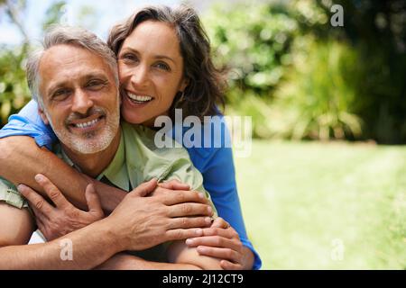 We fill each others lives with joy. A cropped portrait of an affectionate mid adult couple sitting in their garden on a sunny day. Stock Photo