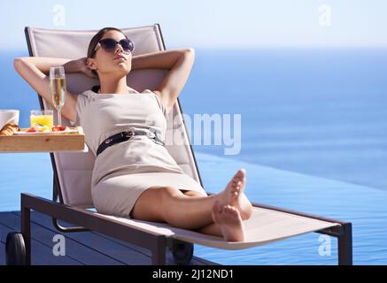 Relaxing while on holiday. A posh young woman reclining on a deck chair with her hands behind her head. Stock Photo