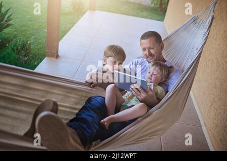 Swinging along to a chilled weekend with the kids. Shot of a father and his two little children using a digital tablet while relaxing on a hammock Stock Photo