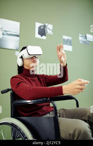 Young Asian man with disability wearing VR headset visiting contemporary photography exhibition in modern art gallery using augmented reality technolo Stock Photo