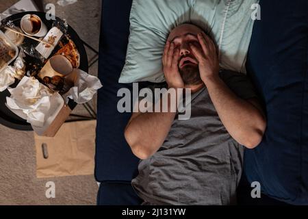 Depressed frustrated man in despair laying on couch, feeling irritated about solitude and loneliness. Desperate sad adult with chronic depression difficulties having disappointment crisis. Stock Photo