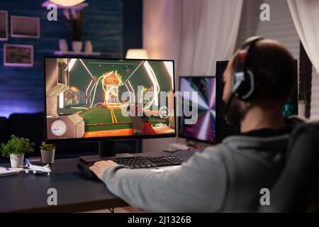 Person playing video games with controller on computer. Player using  joystick and wearing headphones to play online game on monitor. Modern man  using gaming equipment to have fun. Stock Photo