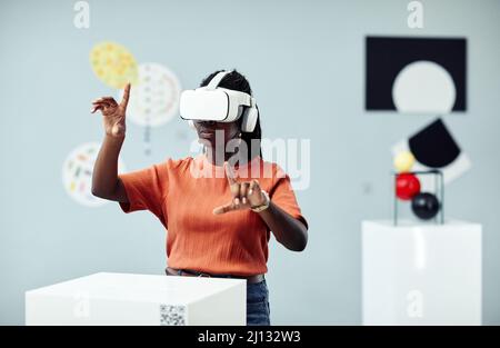Young African American woman wearing VR headset looking at art objects at contemporary exhibition using augmented reality technology Stock Photo