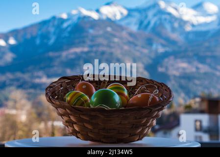 close up exposure of handmade easter basket with colorful easter eggs in a nest and wonderful snowy mountain backdrop in the tyrolean alp Stock Photo