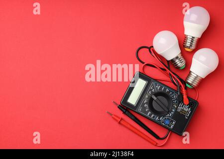 Multimeter and energy saving bulbs on red background Stock Photo