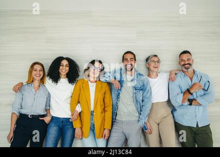 Happy businesspeople smiling cheerfully while standing together against a wall. Group of successful entrepreneurs working together as a team in a mode Stock Photo
