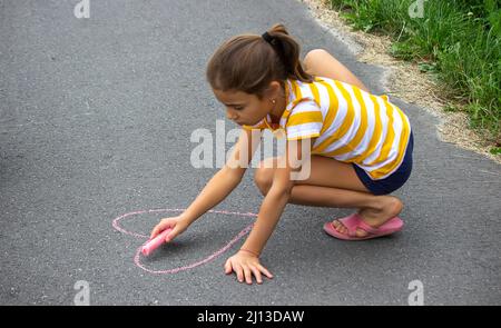 the child draws with chalk on the pavement, the heart is the sun. Nature. selective focus Stock Photo