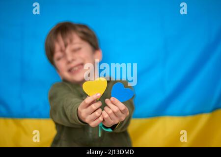 Boy hands holding yellow-blue paper hearts on Ukrainian flag background. Kids support Ukraine, stop war, stay with Ukraine hashtag Stock Photo