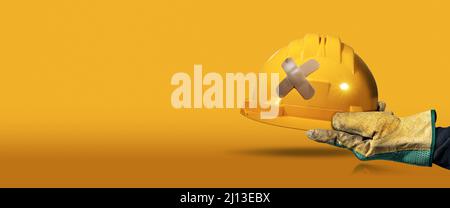 Manual worker with protective work glove holding a yellow safety helmet with a cross bandaid (adhesive bandage), on a yellow and orange background. Stock Photo
