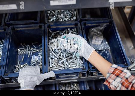 Above angle of gloved hands of female machinery builder holding pile of bolts made up of stainless steel while working in warehouse Stock Photo