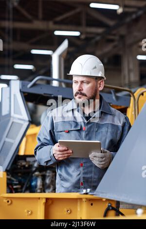 Serious mature male worker of quality control management department using tablet while testing new industrial machinery Stock Photo