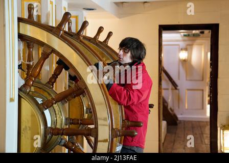 Student conservator Andrew Braund from West Dean College, cleans the helm of the Victorian battleship HMS Warrior at Portsmouth Historic Dockyard, as part of National Spring Cleaning Week. The conservation team have been researching and trialling a different way to treat the brass, using less abrasive techniques and a coating system that works well with the environment. Launched in 1860, HMS Warrior was Britain's first iron-hulled warship and had a lasting influence on naval architecture and design. Picture date: Tuesday March 22, 2022. Stock Photo